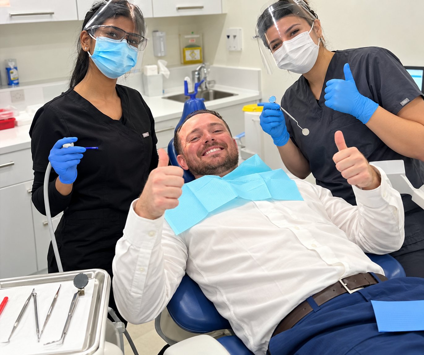 A patient in the dental chair giving a thumbs up with two smiling clinicians beside him